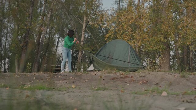 Person packing tent after campsite, folding fabric and stowing poles into bag, securing straps and checking stakes soft dusk light, birch trees and clearing, quiet departure mood across frames showing
