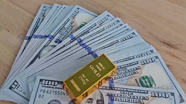 Large stack of 100 dollar bills with gold bar on wooden table
