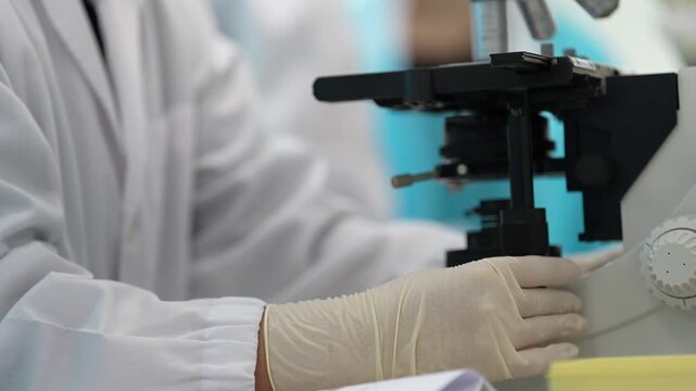 Laboratory microscope in clinical lab with gloved scientist hand, white coat, medical research analysis, sterile equipment, close up, blurred background and examination sample in clean laboratory