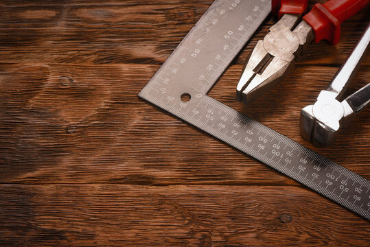Metal square ruler and hand tools in flat lay composition on wooden workbench table background with copy space.