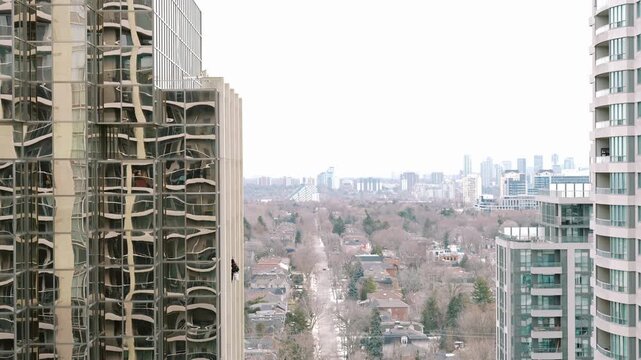 Suspended technician performing exterior cleaning on skyscraper with distant city and clouds as background