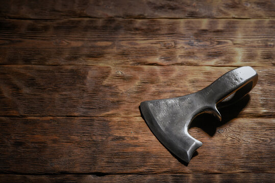 Forged medieval axe head placed on dark wooden workbench table top view background.