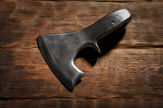 Forged medieval axe head placed on dark wooden workbench table top view background.