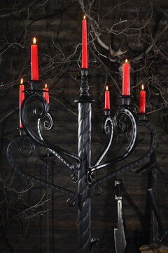 Forged wrought iron floor candelabras with twisted columns and lit red candles in dark medieval castle stronghold interior.