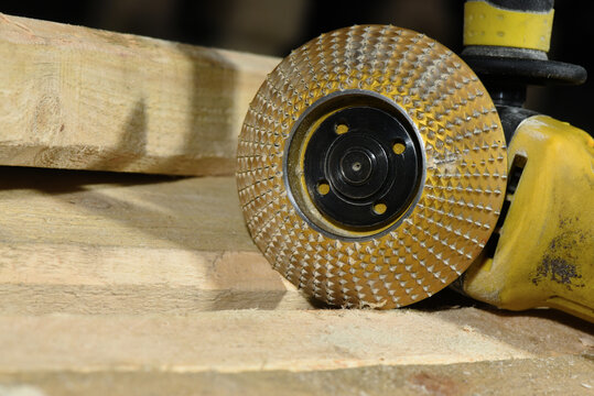 Electric angle grinder with carbide rasp disc placed on light stone blocks on workshop surface with dark close up background.