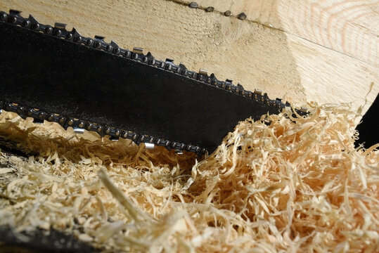 Chainsaw cutting wooden beam with fresh sawdust pile in workshop environment close up background.