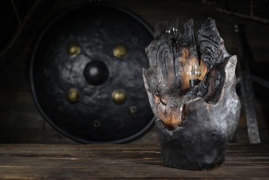 Carved wooden candle holder made from burned tree log with embedded glowing electric candles bulb emitting warm red light in dark atmospheric interior.