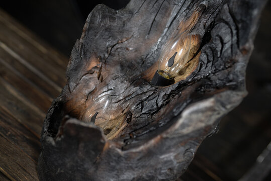 Carved wooden candle holder made from burned tree log with embedded glowing electric candles bulb emitting warm red light in dark atmospheric interior.