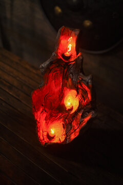 Carved wooden candle holder made from burned tree log with embedded glowing electric candles bulb emitting warm red light in dark atmospheric interior.