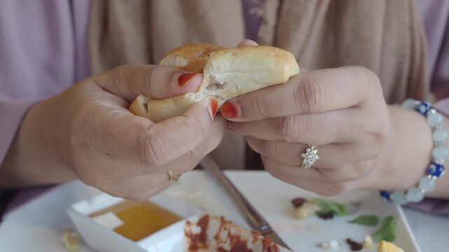 Close-up of a woman breaking fresh bread during a meal, symbolizing eating habits, bakery food, dining experience, breakfast, lunch, and food culture.