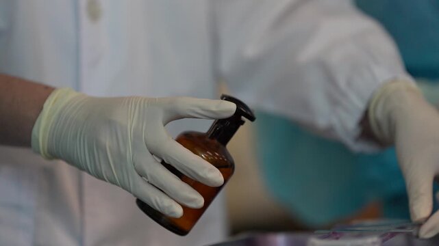 Gloved hand holding glass bottle and staining slide in laboratory with scientist medical research sample preparation and microscope work