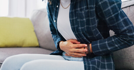 Obraz premium Woman, hands and sofa with stomach ache in home for menstruation, pain or period cramps. Female person, sore belly and indigestion with gastrointestinal reflux or discomfort for IBS or constipation