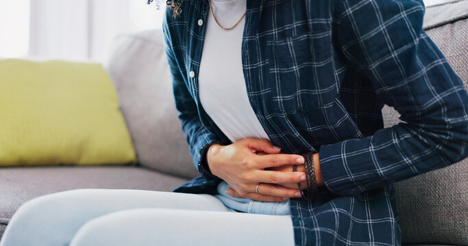Woman, hands and sofa with stomach ache in home for menstruation, pain or period cramps. Female person, sore belly and indigestion with gastrointestinal reflux or discomfort for IBS or constipation