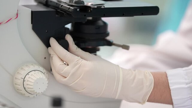 Laboratory microscope gloved hand medical equipment research laboratory scientific instrument close up white glove technician specimen stage focus knob clinical analysis biology testing lab
