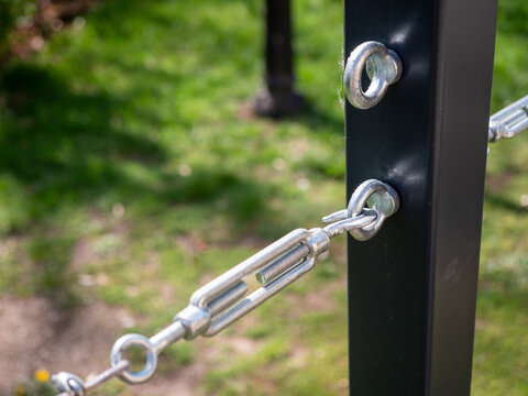 Close-up of a turnbuckle attached to a steel post, metal connection, structural component used for tensioning and stabilizing cable systems.