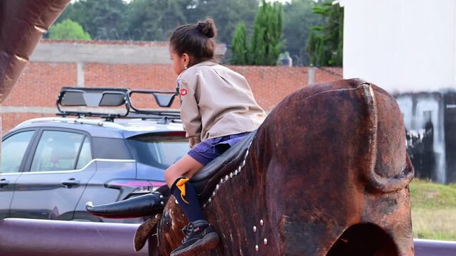 Girl scout riding mechanical bull.