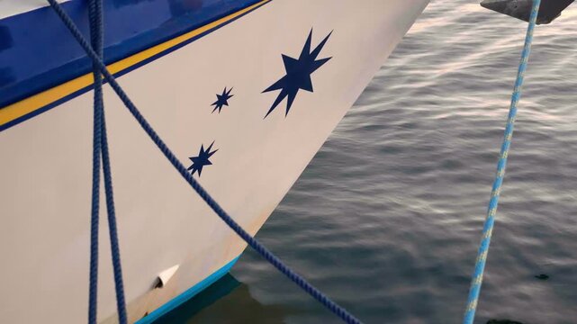 Ship hull featuring blue stars and rigging ropes in the harbor of Santa Cruz de Tenerife. Blue rippling sea water in the background. Static shot.
