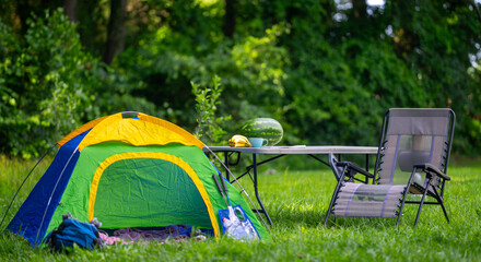 Camping tent set in green nature for outdoor summer leisure. Cozy camping setup with tent, chair, and table in the countryside. Outdoor camping scene with picnic. Summer vacation. © Volodymyr