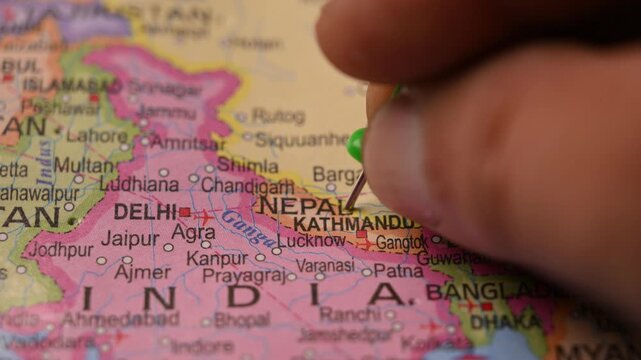Man Marking Nepal Location with Green Pin on Paper World Map in 4K 60fps Close-Up Travel Concept