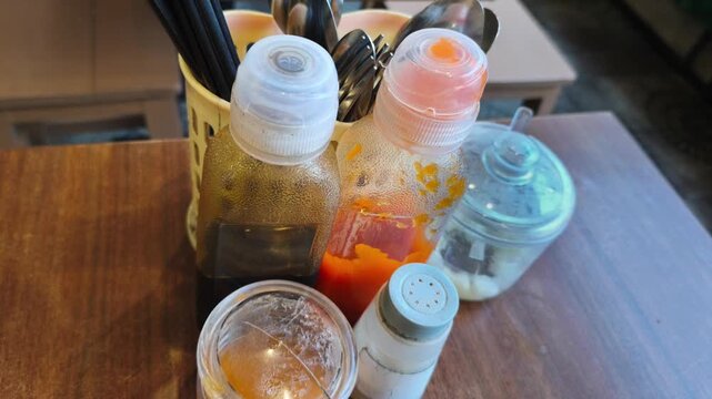 Authentic Indonesian street food condiments and cutlery set on a wooden restaurant table, capturing the vibrant local dining culture through a close-up shot of traditional sauces and spices.