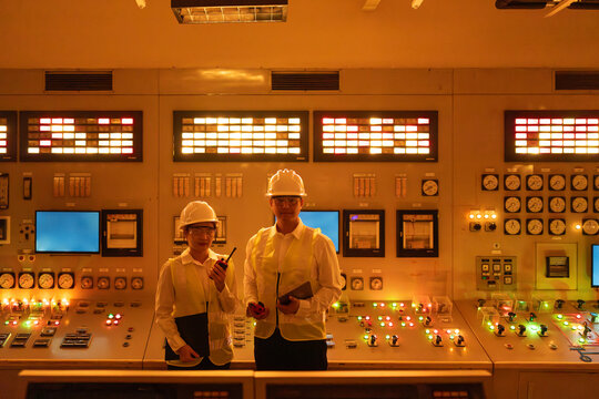 Asian engineers operating control systems in nuclear energy power plant control room, monitoring  energy production, advanced technology, safety systems and world class industrial operations concept