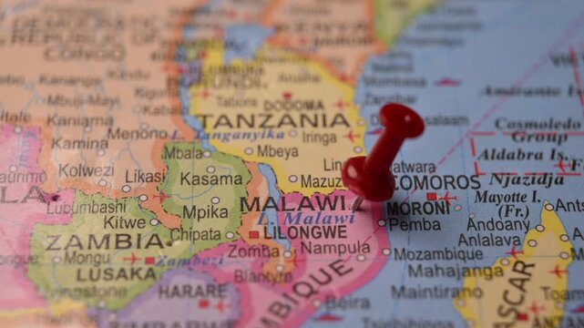 Man Marking Malawi Location with Red Pin on Paper World Map in 4K 60fps Close-Up Travel Concept