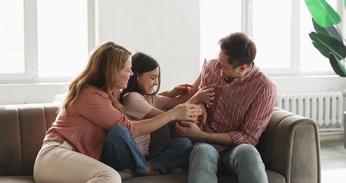 Loving parents and child daughter tickling during leisure in living room, family sitting on sofa, having fun, laughing, playing together at home. Happy parenthood, bonding, playful interaction indoors