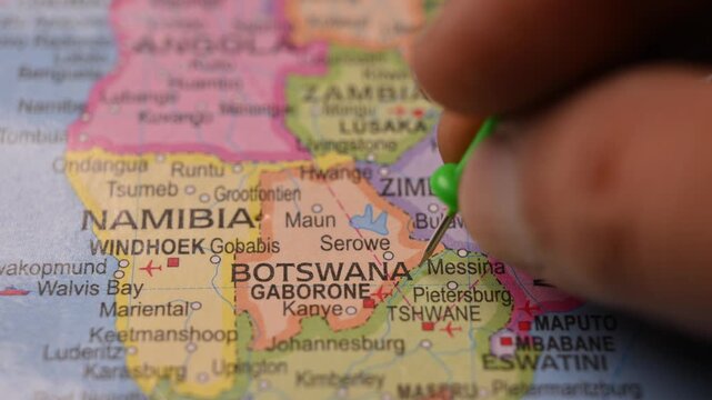 Man Marking Botswana Location with Green Pin on Paper World Map in 4K 60fps Close-Up Travel Concept