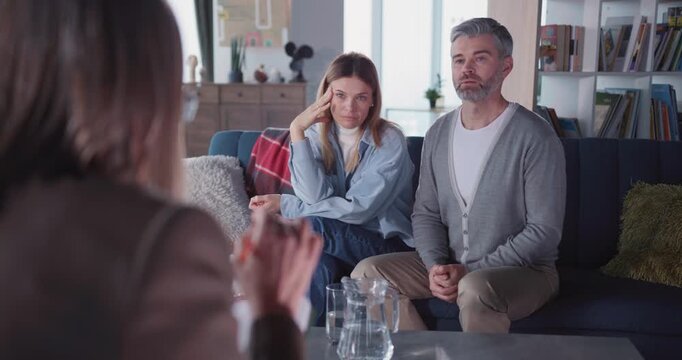 Caucasian adult couple listening to psychologist doctor advice inside apartment. Family therapist woman explaining relationship problems to married people.