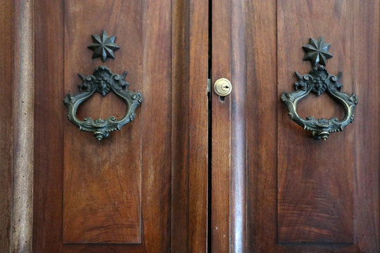 Dettaglio di antico portone in legno massiccio con coppia di battenti classici in metallo brunito, architettura storica italiana e design rustico vintage di un ingresso monumentale
