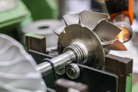 ​A close-up shot of a turbocharger turbine wheel mounted on a shaft during a high-precision dynamic balancing procedure in a specialized workshop.