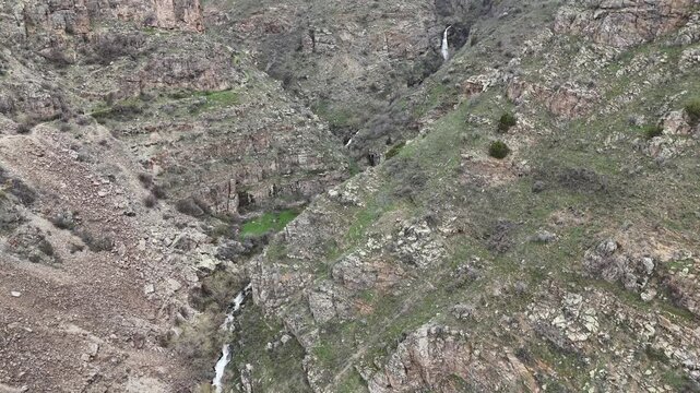 4K aerial drone footage of rocky mountain canyon with stream and small waterfall, natural landscape.