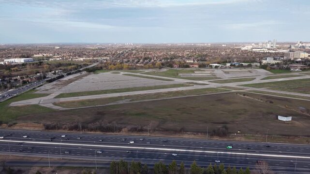 A wide aerial shot of the decommissioned Buttonville Municipal Airport runways with heavy vehicle traffic flowing on the adjacent Highway 404 in Markham, Ontario
