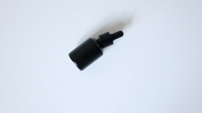 Black bottle with a pipette isolated on a white background. Photo. The bottle is half-open. Placed in the middle of the background, casting a shadow. Oil, serum, care product. Medicine, beauty, health