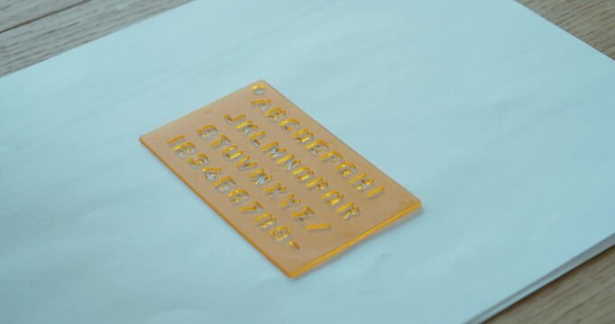 Hand positioning a stencil on paper, representing structured writing, learning, and precision.