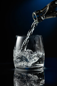 Crystal clear vodka being poured over ice in a glass.