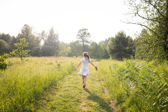 girl child is running along road in summer in nature through field and forest