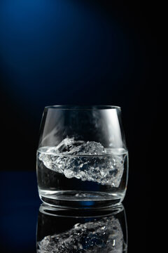 Vodka with ice on a black reflective background.