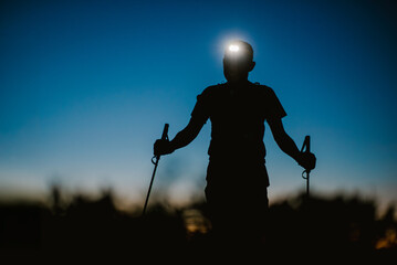Silhouette of a Male Trail Runner with Headlamp and Trekking Poles at Dusk © febmotion