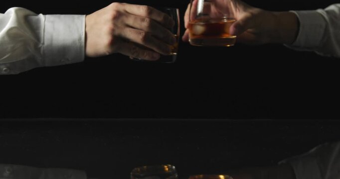 Close-up of people holding glasses of whiskey ready to clink in a minimal black background scene.