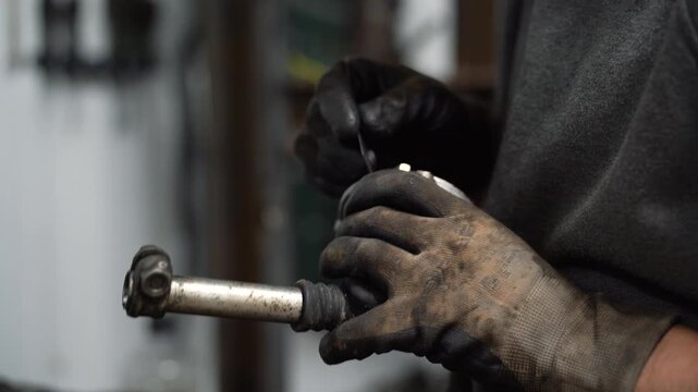 A mechanic cleans car parts by cutting off excess glue from a gearshift lever.