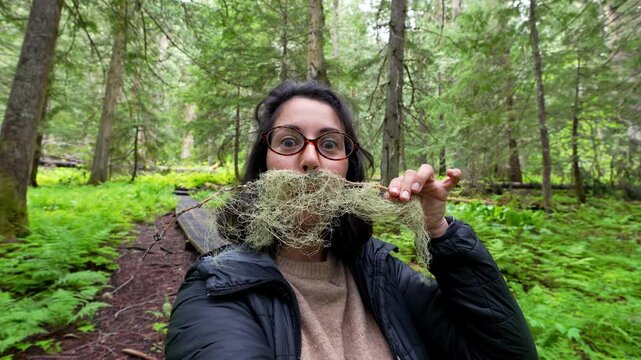 Woman making a funny mustache with usnea lichen during forest hike