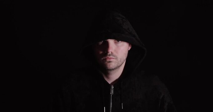 Man in a dark hoodie walking toward the camera, creating a mysterious and threatening atmosphere.