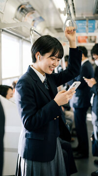 電車内でスマートフォンを見て笑顔で通学する女子高校生