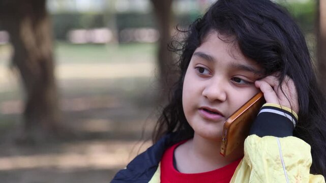 A young Indian girl having a phone conversation in a calm natural environment, showing childhood innocence, communication, and simple slum village poor india lifestyle in a mountain rural setting