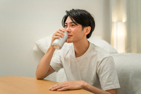 A young Asian man drinking canned beer and canned chu-hi (a type of Japanese alcoholic beverage) at night in his bedroom at home.
