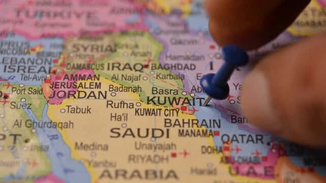 Man Marking Kuwait Location with Blue Pin on Paper World Map in 4K 60fps Close-Up Travel Concept