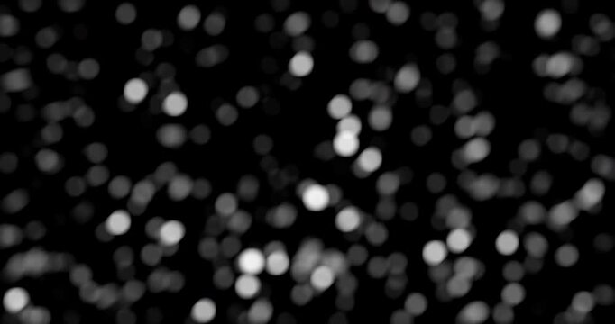 White particles drift across a black background resembling snow or dust in slow motion.