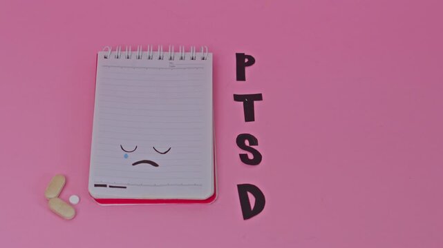 Stop motion animation of PTSD letters appearing beside sad face notebook and pills on pink background