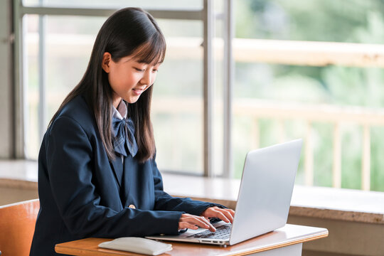 Female middle and high school students in their school uniforms studying using computers.